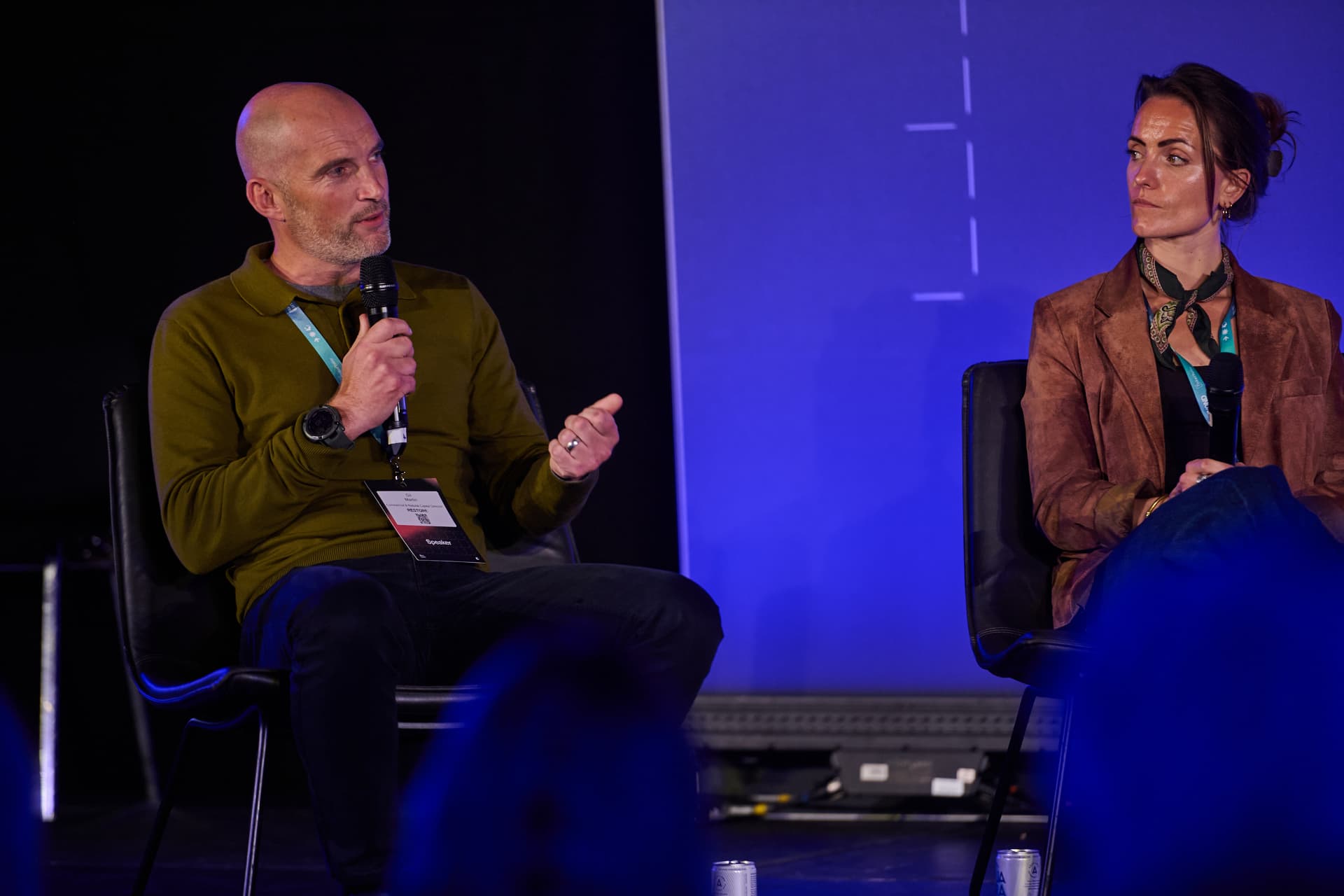 Gil Martin speaking into a microphone on a conference panel, seated beside a fellow panellist and seen from the audience